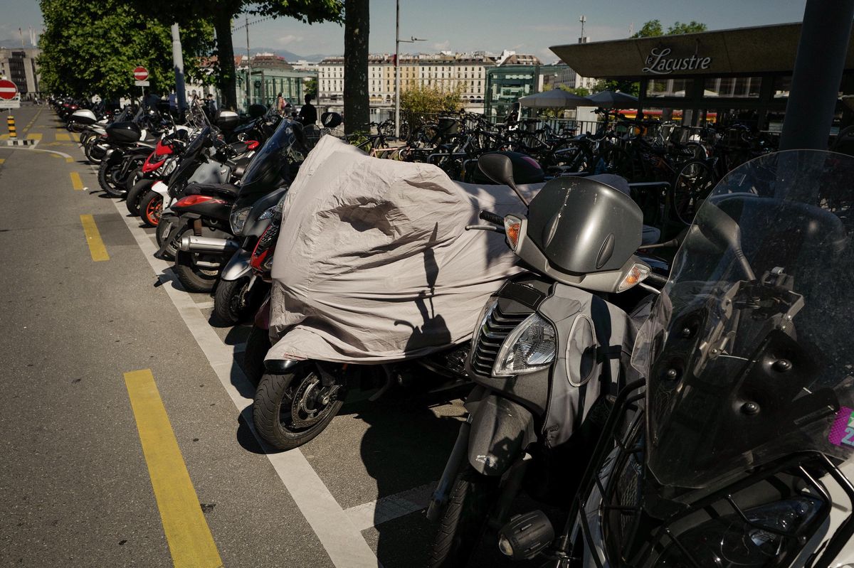 Scooters et motos garés le long du quai Général-Guisan à Genève, avec un scooter couvert au premier plan. Photo prise le 30 juin 2022.