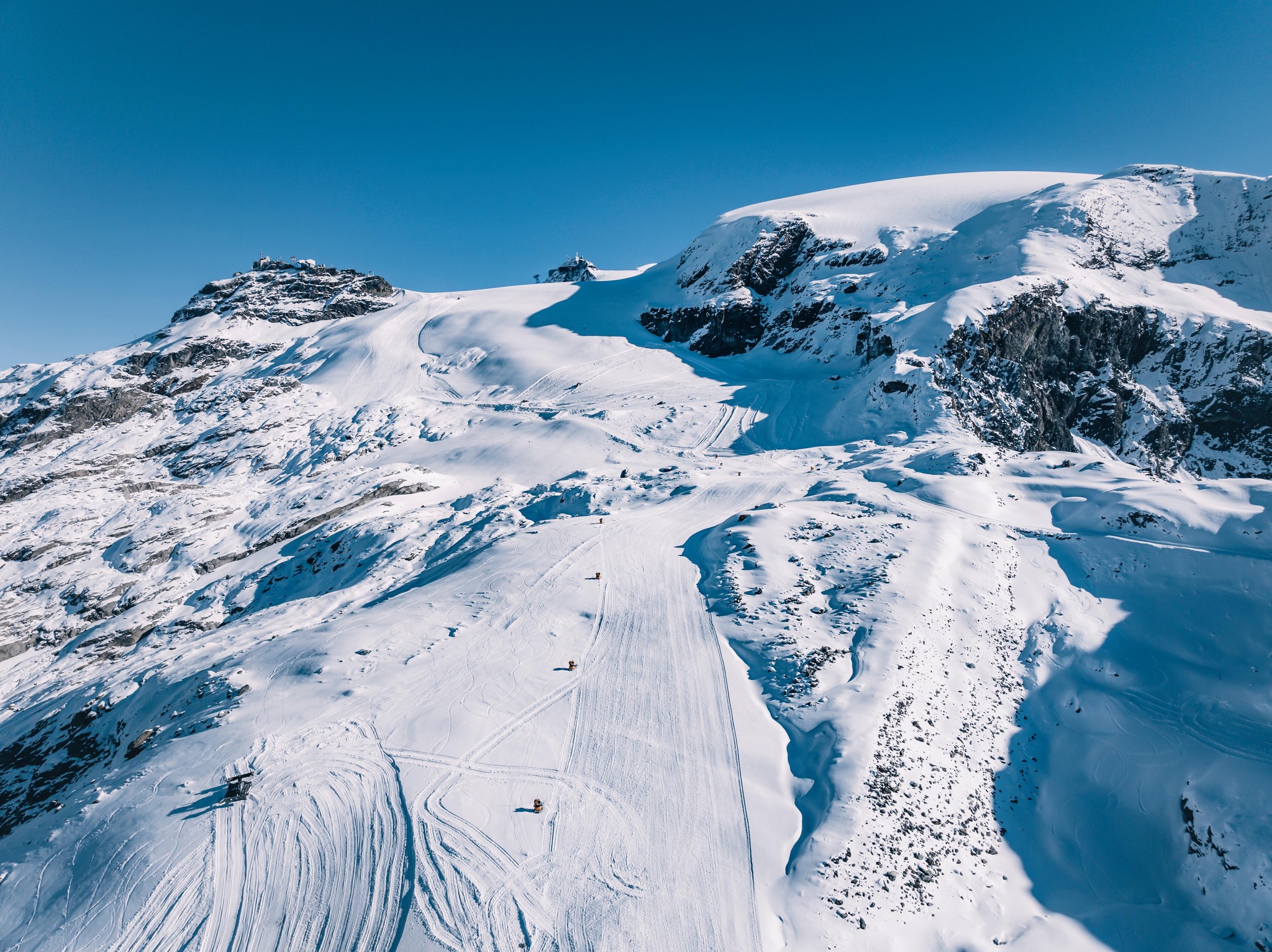 Verschneite alpine Landschaft mit Skispuren unter klarem blauem Himmel.