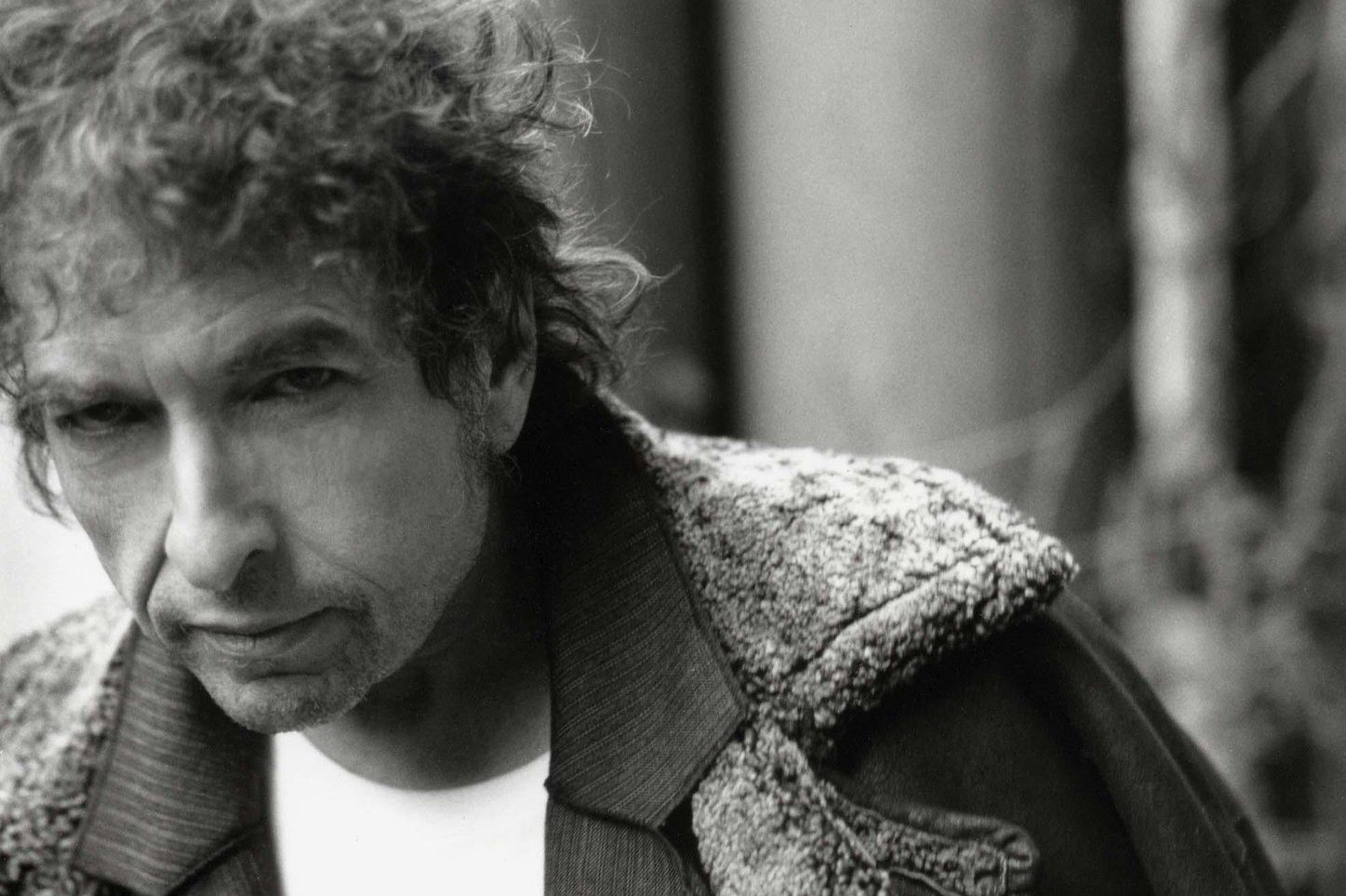 Homme avec une veste en laine tenant une canne, posant avec un air pensif.