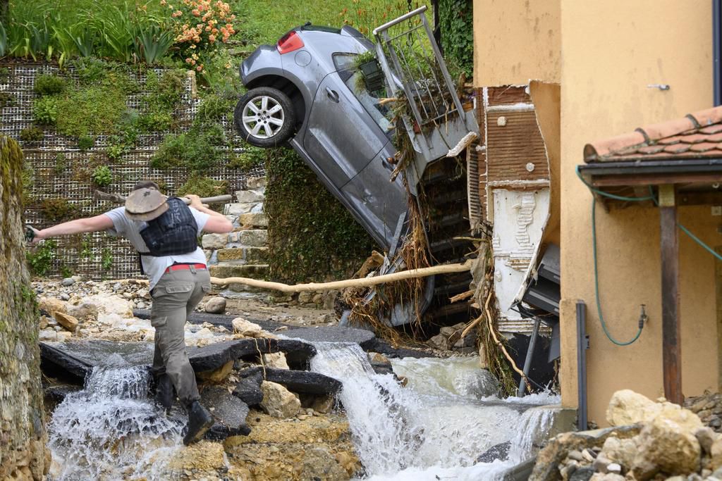 Une personne marche avec des pelles à côté d’une carcasse de voiture bloquée a la verticale contre une maison après un violent orage ce mercredi 23 juin 2021 à Cressier. Ce mardi soir 22 juin 2021 vers 19h00, de violentes intempéries ont provoqué la crue du Ruhaut et d’importants dégâts dans le village de Cressier et de Frochaux. La police neuchâteloise et les forces d’intervention du Canton de Neuchâtel ont œuvré toute la nuit afin de stabiliser la situation.