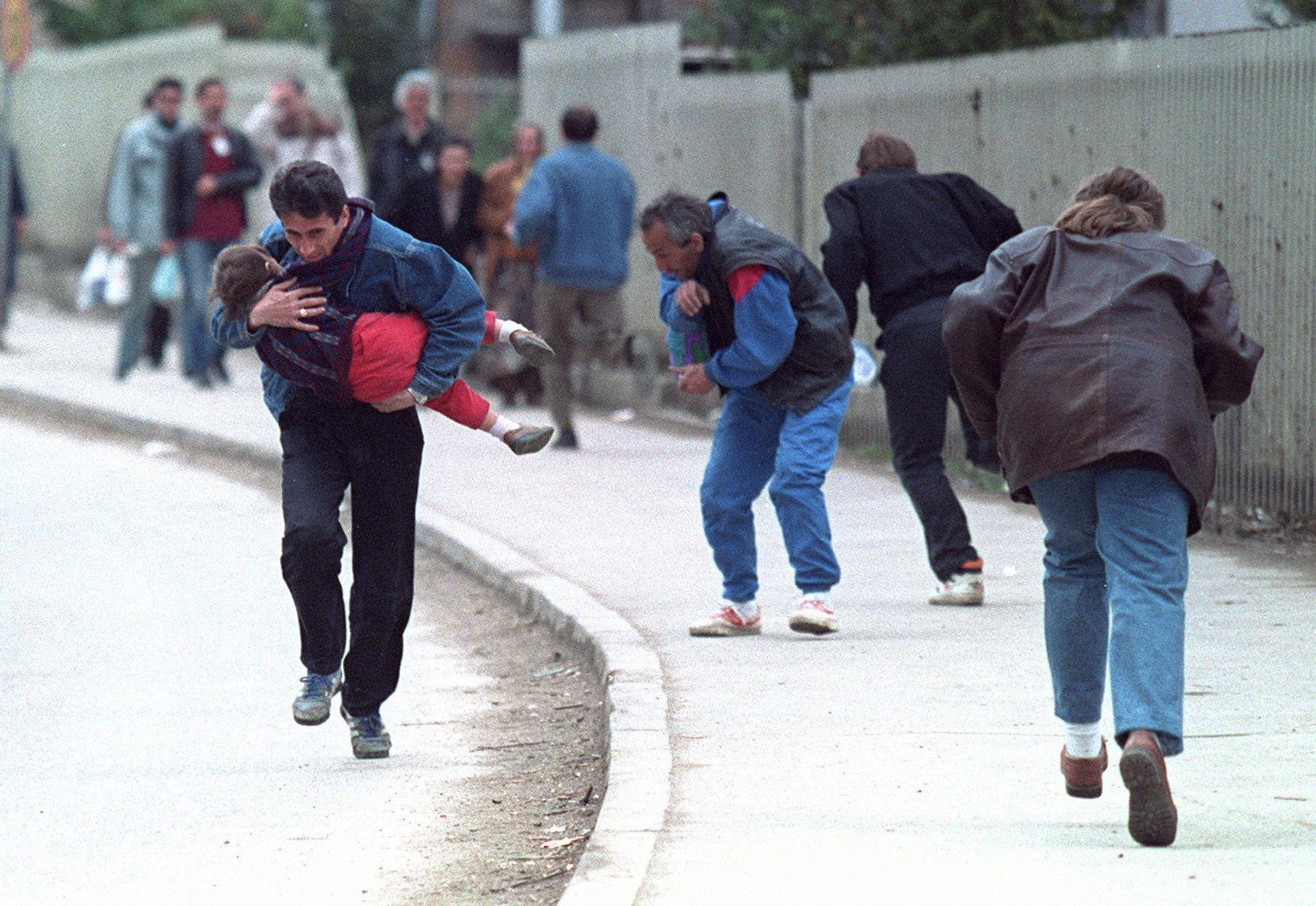 Ein bosnischer Mann trägt im April 1993 sein Kind, während sie und andere an einem gefährlichen Scharfschützengebiet in Sarajevo entlanglaufen.