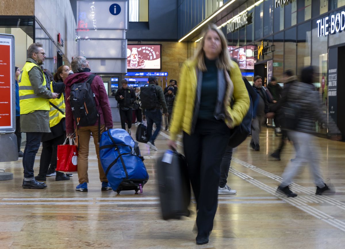 Passagers avec bagages dans une gare animée entre Genève et Lausanne, perturbation du trafic ferroviaire.