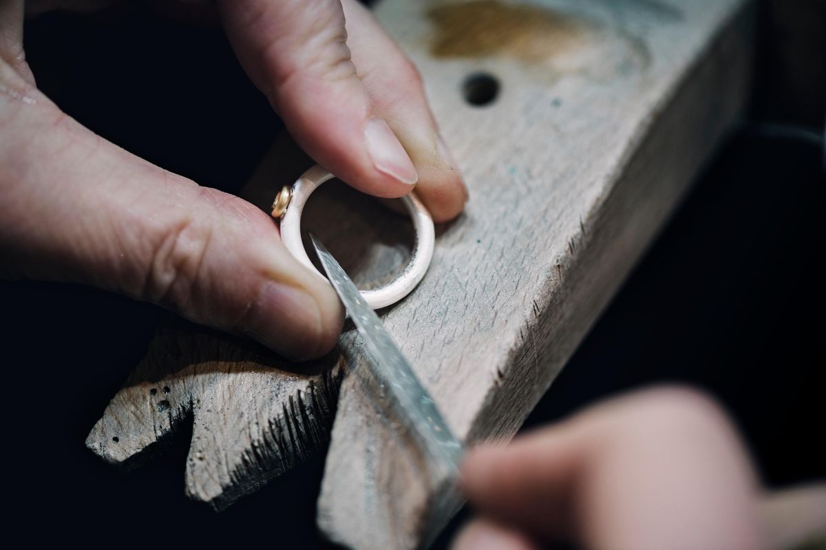 Gros plan des mains d’une orfèvre professionnelle limant un sertissage en or pour un diamant sur une bague en argent, dans son atelier à Møn, Danemark.
