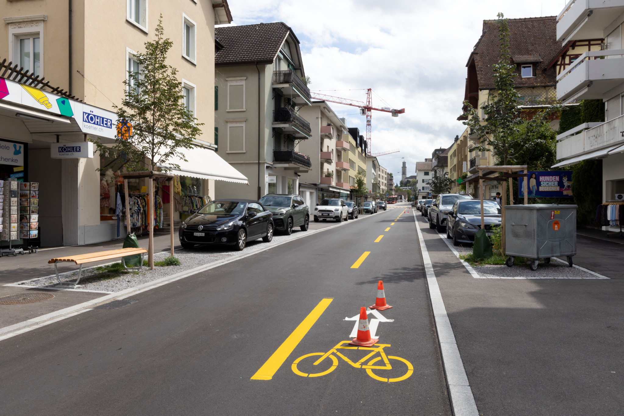 Sanierte Gotthardstrasse in Thalwil mit Velostreifen, Leitbaken, neuen Bäumen und Sitzbänken entlang der Ladenzeilen.