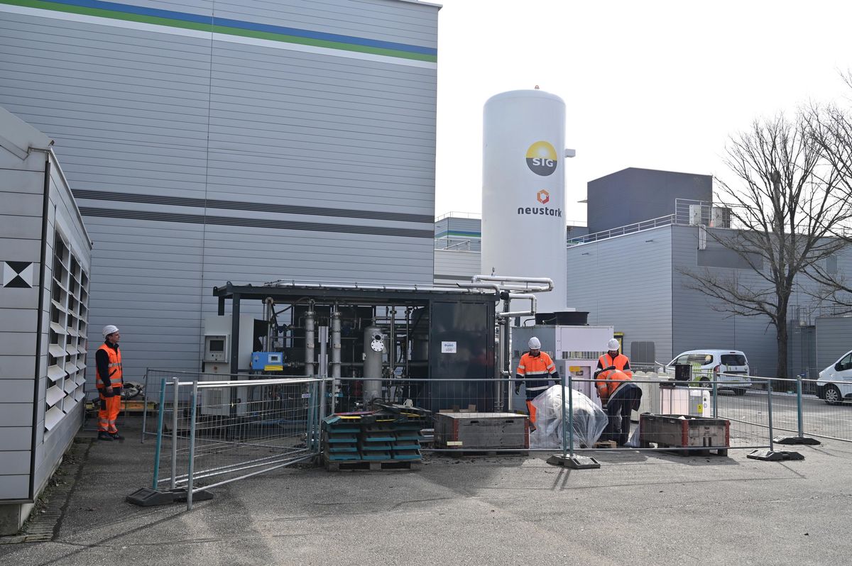 Travailleurs en tenue orange près d'un appareil de capture de CO2 devant un bâtiment industriel.