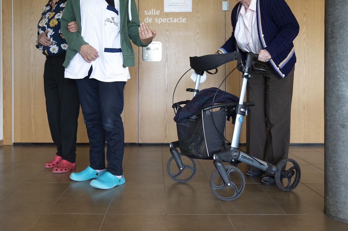 Personnes aidant un résident avec un déambulateur dans un EMS à Cheseaux, bilan après un an de COVID.