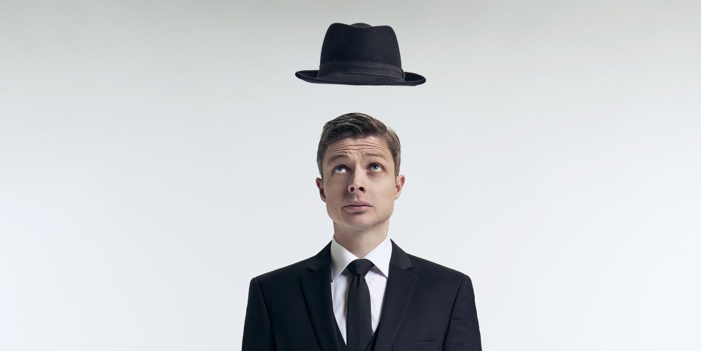 Un homme en costume noir debout avec un chapeau flottant au-dessus de sa tête.