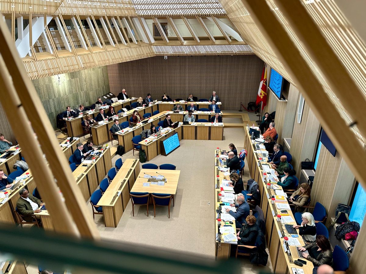Vue d’une salle de réunion avec des personnes assises autour de plusieurs tables disposées en forme de U, lors d’une séance plénière.