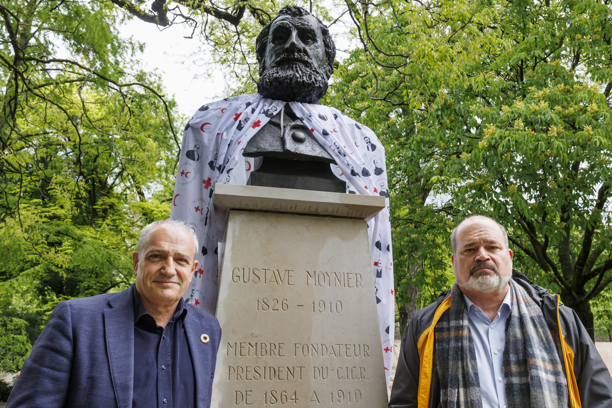 Alfonso Gomez, gauche, maire de Geneve, et Sami Kanaan, droite, conseiller administratif de la ville de Geneve, posent vers le buste Gustave Moynier, portant une cap a l'occasion de la journee mondiale du CICR, dans le parc des Bastions a l'issue de leur conference de presse sur le plan d'action du Conseil administratif de la ville de Geneve "Monuments et heritage raciste dans l'espace public", ce lundi 6 mai 2024 a Geneve. (KEYSTONE/Salvatore Di Nolfi)