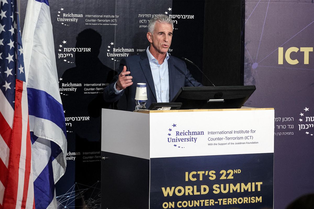 Un homme s'exprime lors du sommet mondial de l'ICT à Herzliya, avec drapeaux et podium visibles.