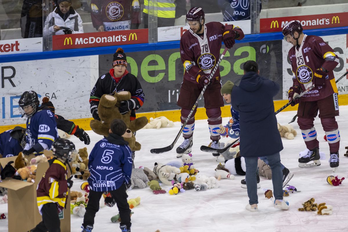 Des enfants et l'attaquant genevois Marc-Antoine Pouliot, gauche, le defenseur genevois Roger Karrer, droite, ramassent des peluches sur la glace des Vernets qui ont ete lancees par les spectateurs, cette operation Peluche est en faveur de l'hopital des enfants des HUG, afin que les joueurs aient les distribues aux enfants malades a L'hopital des enfants, lors du match du championnat suisse de hockey sur glace de National League LNA, entre le Geneve Servette HC et le EHC Bienne, ce samedi 21 janvier 2023 a la patinoire des Vernets a Geneve. (KEYSTONE/Martial Trezzini)