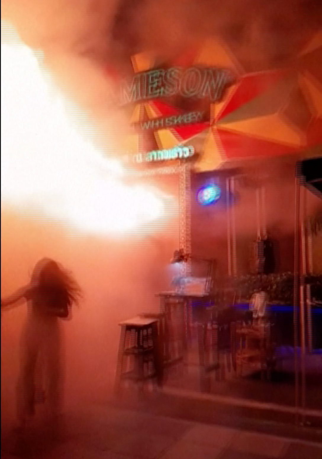 Helle Flammen und Rauch in einer Bar mit einem Jameson Whiskey-Leuchtreklame, eine Person flieht aus dem brennenden Lokal. Helle Flammen und Rauch in einer Bar mit einem Jameson Whiskey-Leuchtreklame, eine Person flieht aus dem brennenden Lokal.