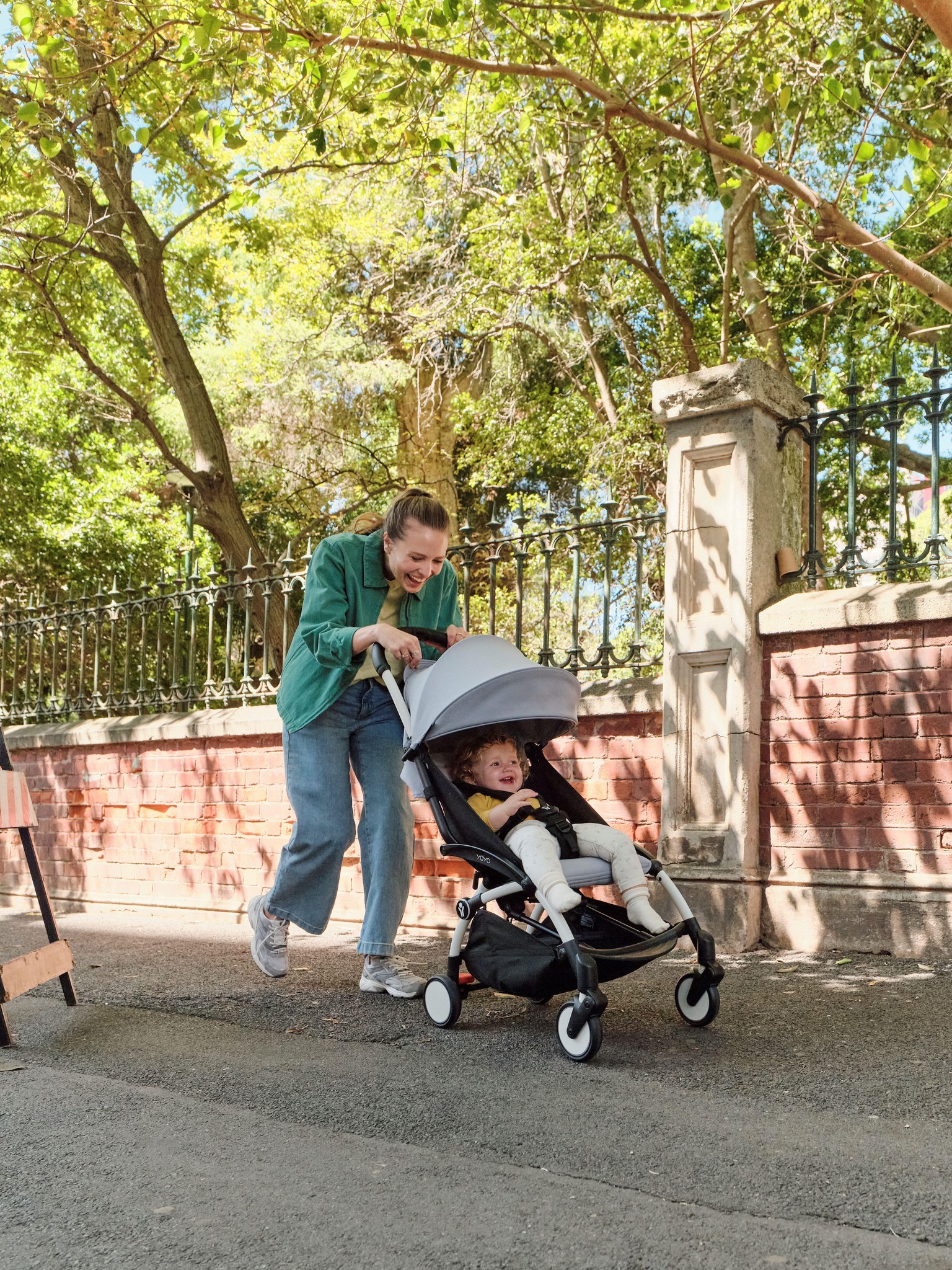 Une mère pousse un enfant dans le nouveau landau Stokke YOYO³ dans une rue arborée.