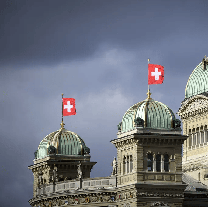 Bâtiment du Palais fédéral suisse avec des drapeaux suisses, sous un ciel nuageux.