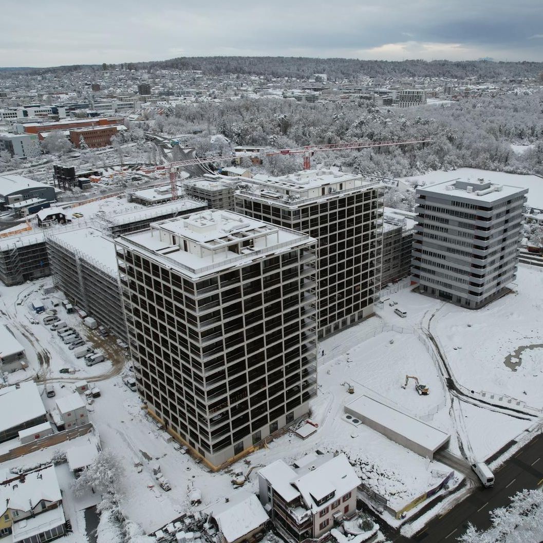 Luftaufnahme eines schneebedeckten Stadtviertels mit modernen Gebäuden in winterlicher Landschaft.