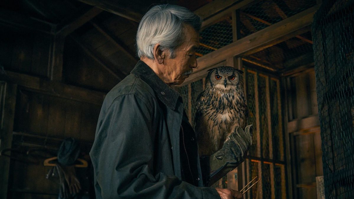 Un homme âgé observe attentivement un hibou perché sur son bras dans un intérieur sombre en bois.