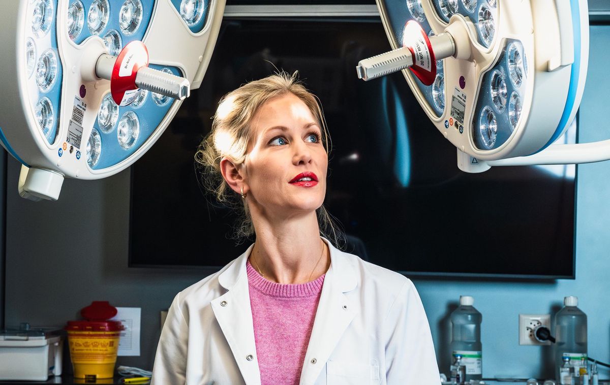 Schönheitschirurgin in einer Zürcher Praxis, umgeben von OP-Leuchten, Blick nach oben gerichtet.