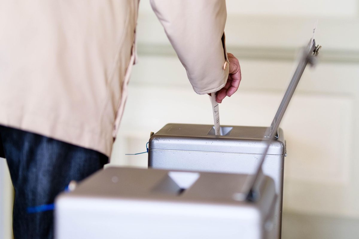 Abstimmungsvorgang in einem Stimmlokal in Bern, Person wirft Stimmzettel in Wahlurne.