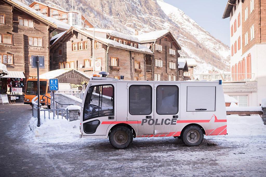 Véhicule de police dans une rue enneigée à Zermatt, Suisse, entouré de bâtiments alpins traditionnels.