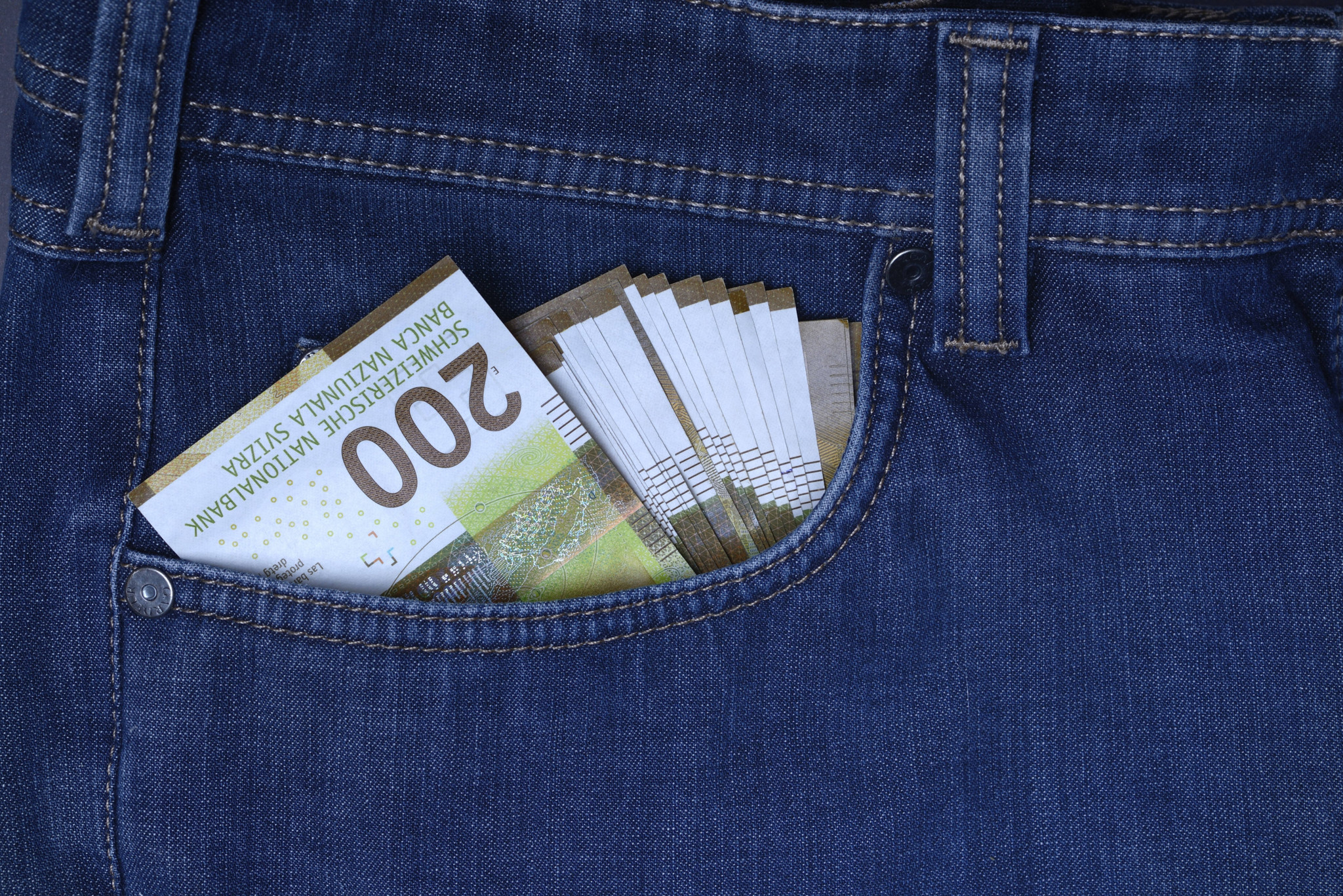 Banknoten von Schweizer Franken stecken in der vorderen Hosentasche einer Jeans.