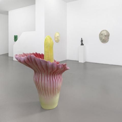 Exposition d’art contemporain avec une sculpture florale audacieuse au centre d’une galerie blanche moderne.