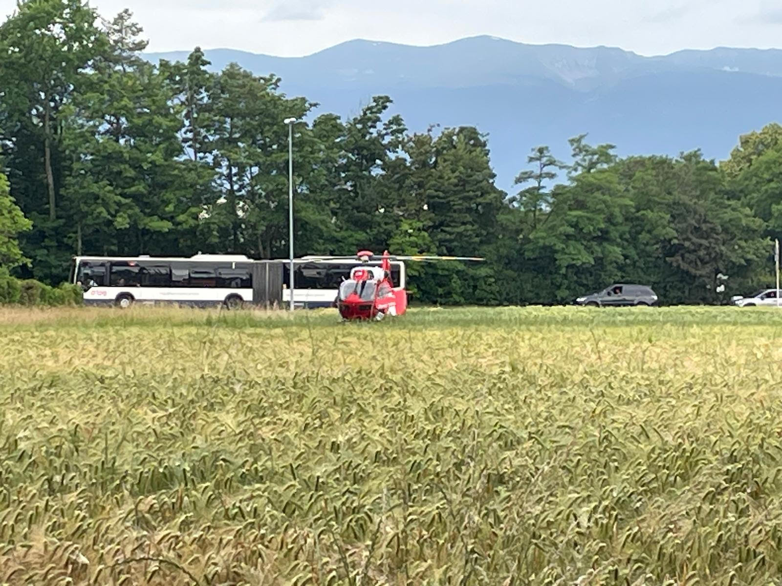 Un hélicoptère de secours rouge posé près d’un bus sur une route, entouré de champs et d’arbres, avec des montagnes en arrière-plan. Un hélicoptère de secours rouge posé près d’un bus sur une route, entouré de champs et d’arbres, avec des montagnes en arrière-plan.