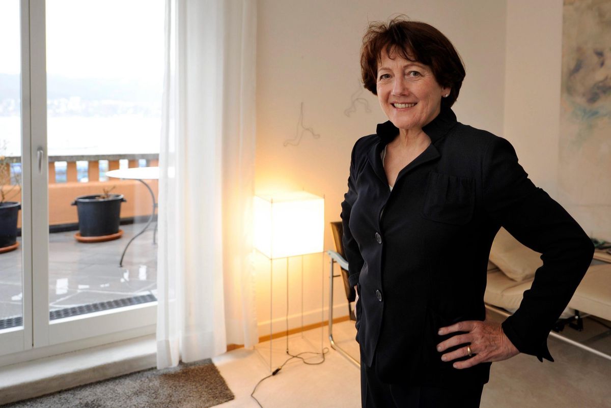 Verena Steiner steht in einem hellen Raum in Zürich, lächelt in die Kamera. Im Hintergrund modernes Kunstwerk und Fenster mit Aussicht.