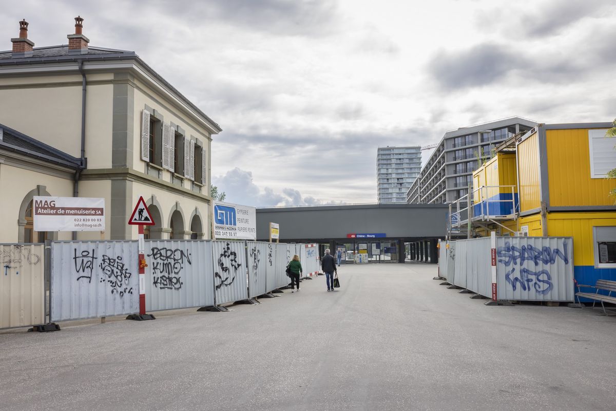 Le principal accès à la gare de Chêne-Bourg se fait en passant entre les palissades de chantiers. A gauche, le bâtiment de l’ancienne gare, destiné à devenir un café-concert.