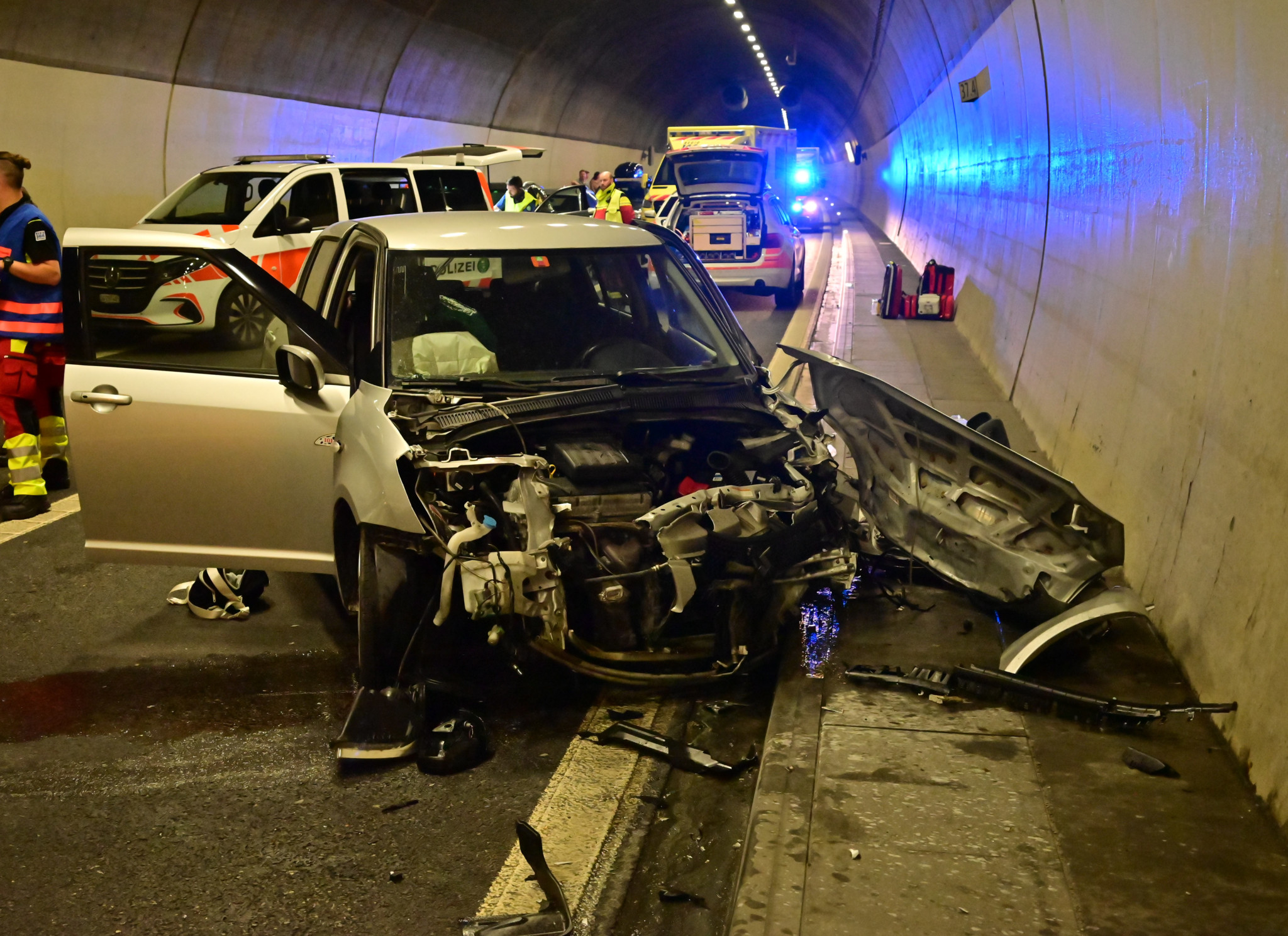 Autounfall in einem Tunnel mit mehreren Rettungsfahrzeugen im Hintergrund und einem stark beschädigten Fahrzeug im Vordergrund.