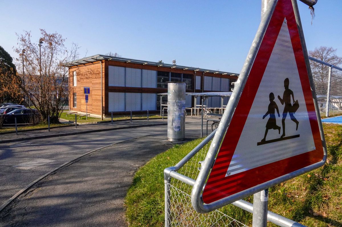 Panneau de signalisation pour enfants près de l’école Pinchat à Carouge, avec un bâtiment en bois en arrière-plan sous un ciel bleu.