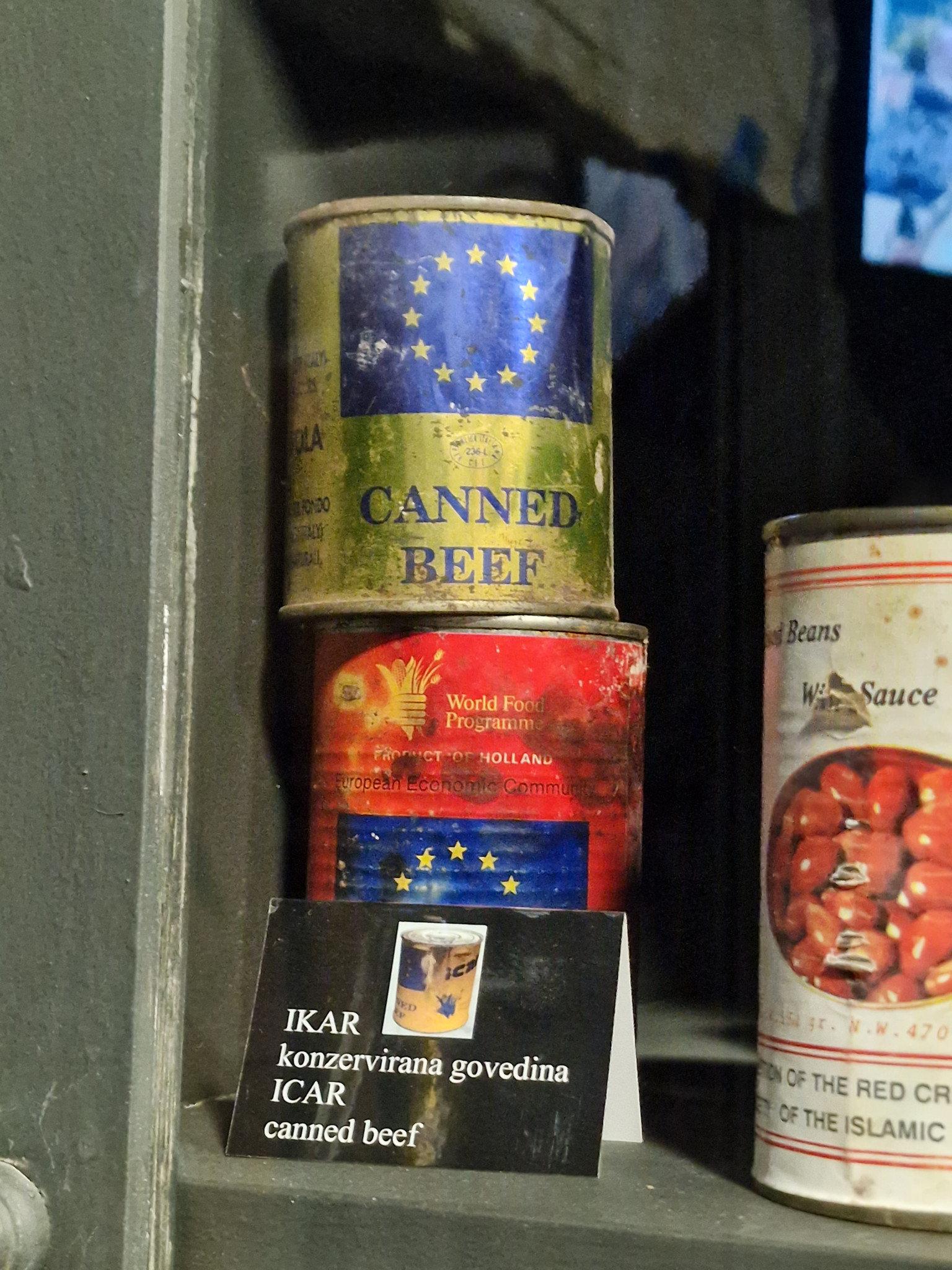 Gestapelte Konservendosen mit der Aufschrift ’Canned Beef’ und EU-Flagge, daneben eine Beschriftung in Englisch und Serbisch.