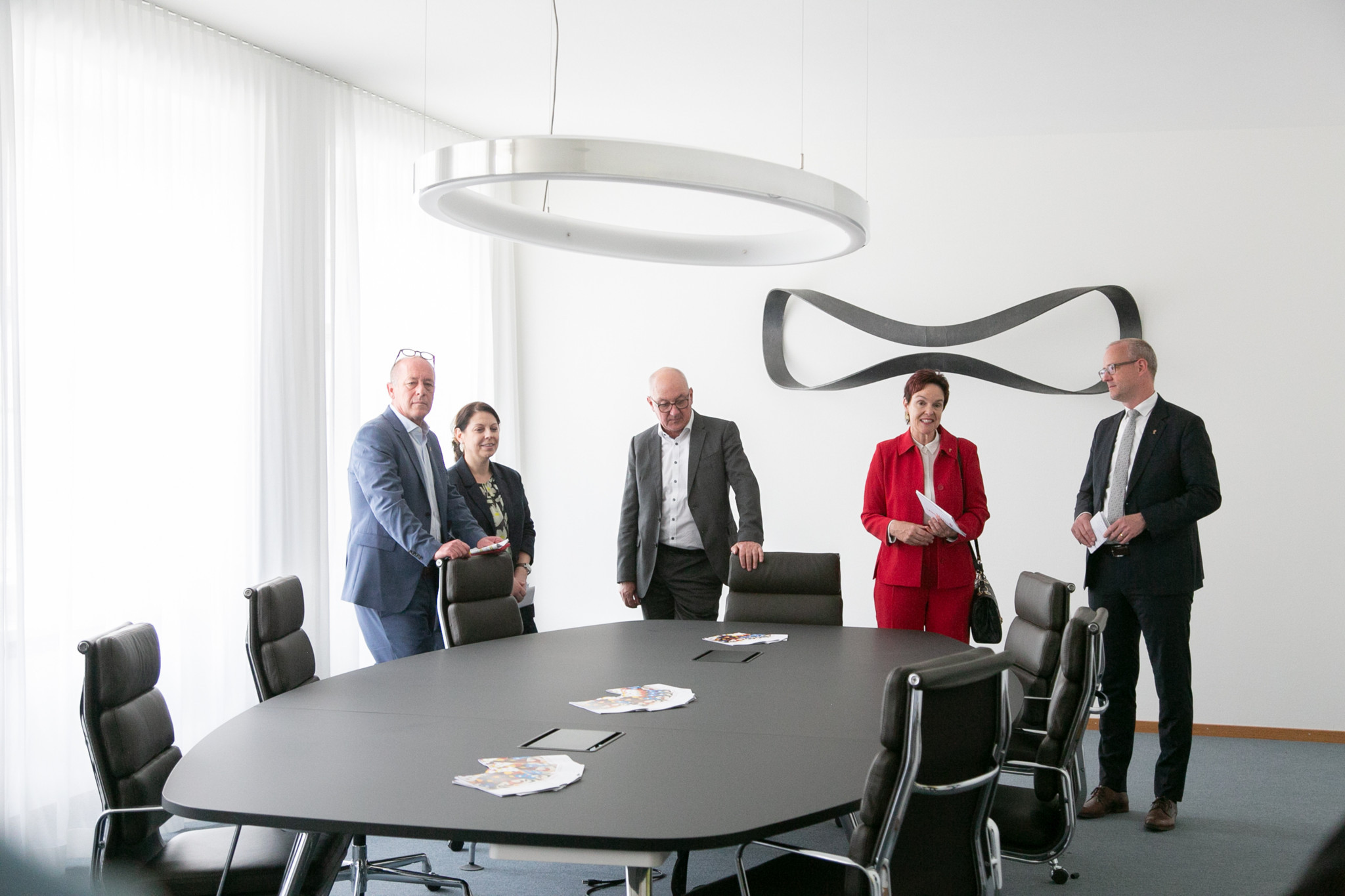 Eine Gruppe von fünf Personen in einem Konferenzraum mit einem ovalen Tisch und modernen Lederstühlen. Eine Gruppe von fünf Personen in einem Konferenzraum mit einem ovalen Tisch und modernen Lederstühlen.