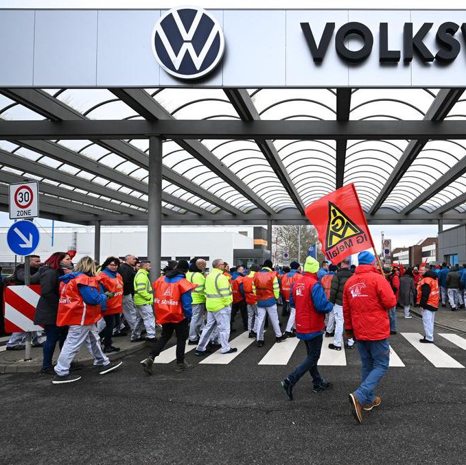 Mitarbeiter von Volkswagen versammeln sich vor dem Werk in Zwickau für einen Warnstreik, organisiert von der IG Metall. Mehrere Personen tragen Gewerkschaftsflaggen und Warnwesten.