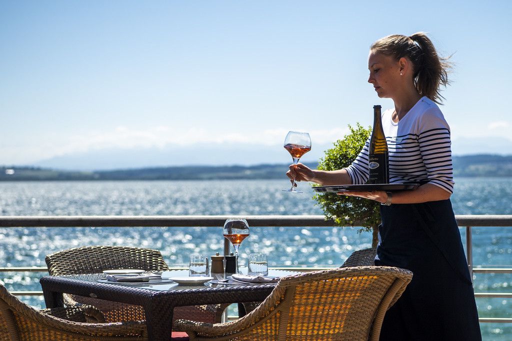 Une femme sert un verre de vin sur la terrasse de l'Hotel Palafitte construit sur pilotis au-dessus du lac de Neuchatel lors de la crise du Coronavirus (Covid-19) le vendredi 29 mai 2020 a Neuchatel. (KEYSTONE/Jean-Christophe Bott)