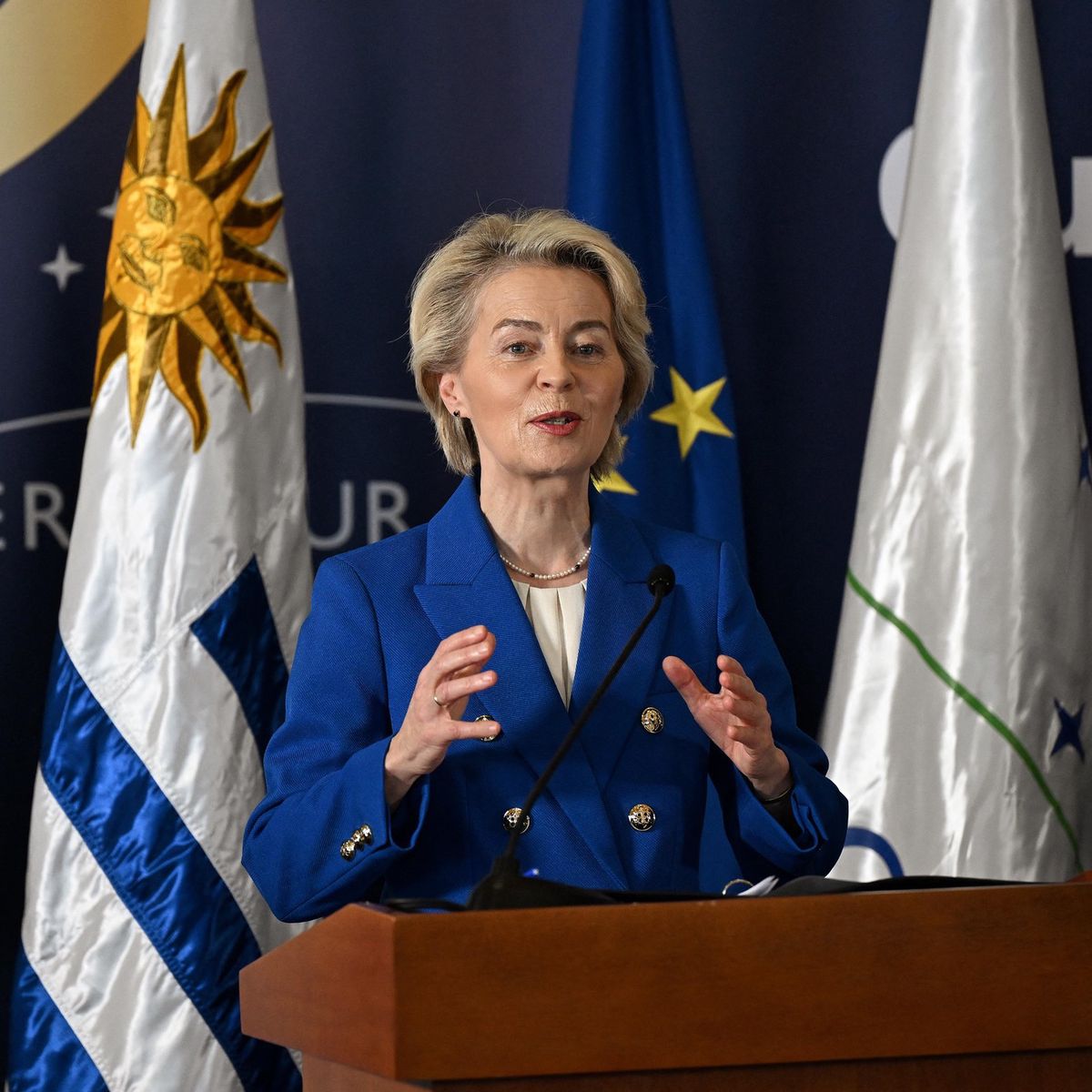 La présidente de la Commission européenne, Ursula von der Leyen, prononce un discours lors du sommet Mercosur à Montevideo, avec des drapeaux en arrière-plan.