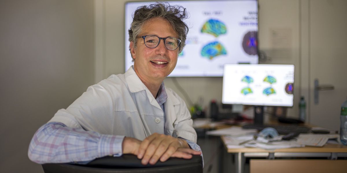 Pr Gilles Allali, chef de service et directeur du Centre Leenaards de la mémoire, assis devant des bureaux avec des écrans affichant des images cérébrales, Lausanne, le 18 mai 2022.