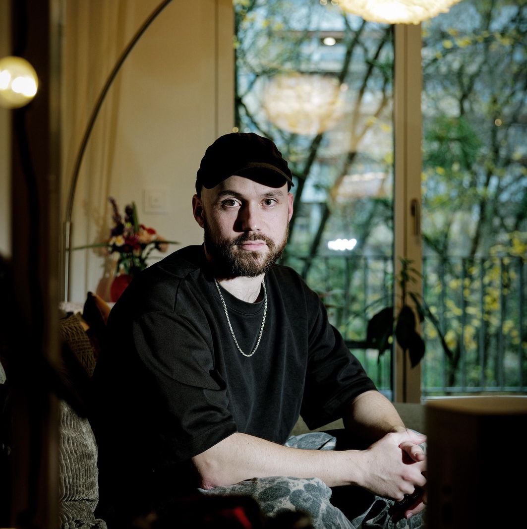 Portrait de Gaspard Sommer, musicien genevois, chez lui à Genève, assis près d’une fenêtre illuminée.