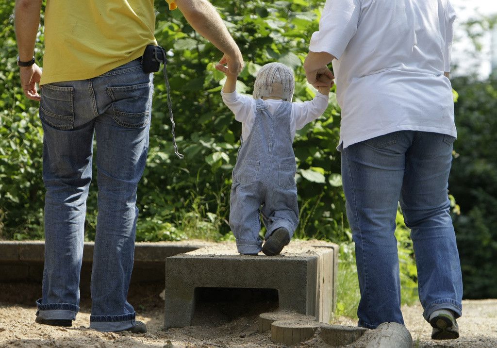 Les parents tiennent les mains de leur petite fille alors qu'ils marchent ensemble dans un parc.