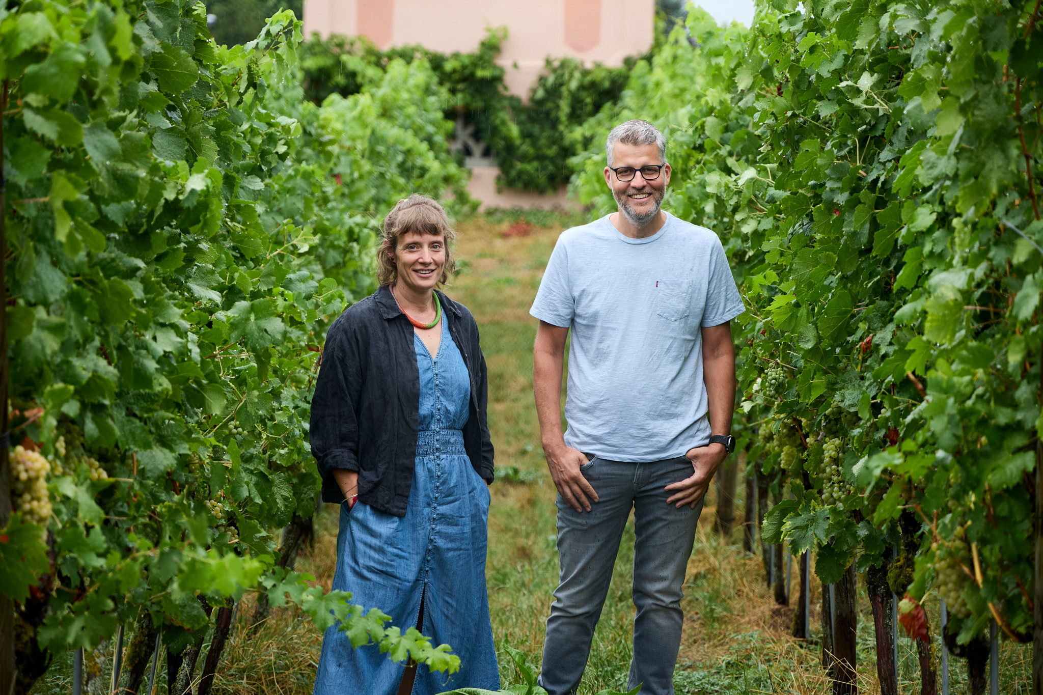 Salome Schneider und Fabio Montalbano, Geschäftsführer des Weinbauzentrums Wädenswil, stehen lächelnd zwischen üppigen Weinrebreihen.