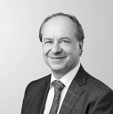 Portrait en noir et blanc d'un homme en costume avec une cravate, souriant légèrement devant un fond neutre.