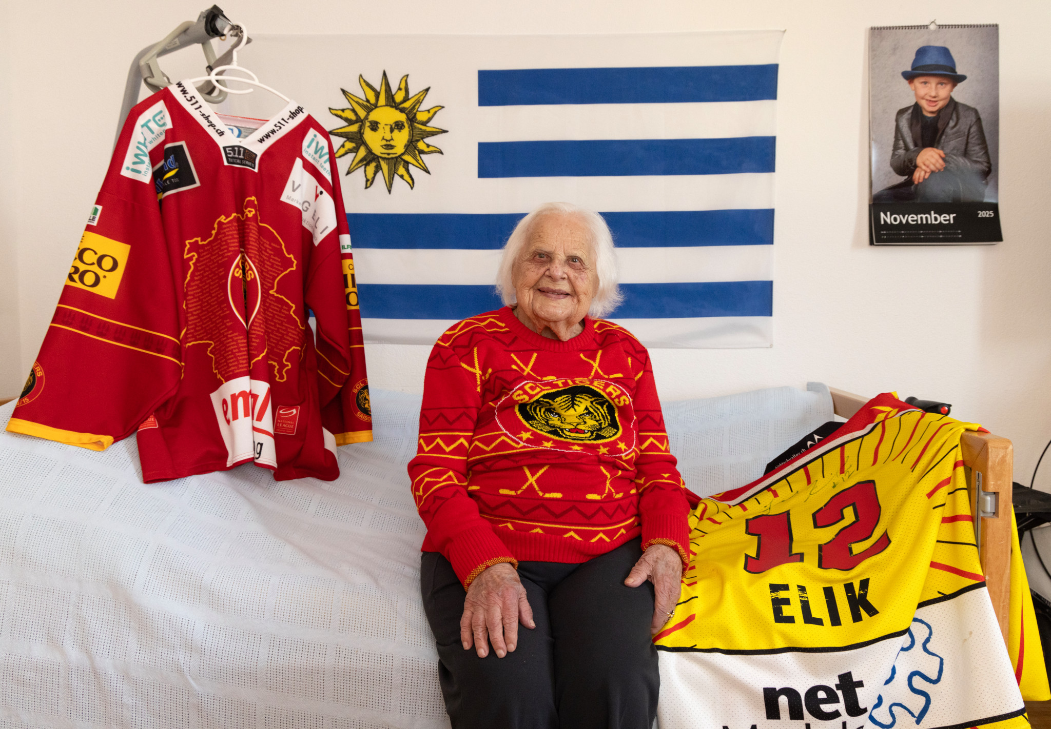 Anna Schmidhauser, 102 Jahre alt, sitzt in ihrem Zimmer im Altersheim Linde mit SCL Tigers-Trikot, umgeben von Fanartikeln.