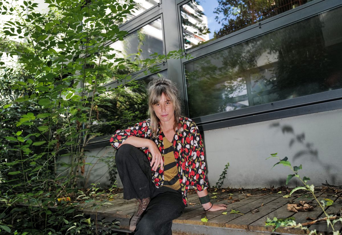 Simone Aubert, musicienne genevoise primée, assise sur une terrasse en bois entourée de verdure devant un bâtiment à Genève.