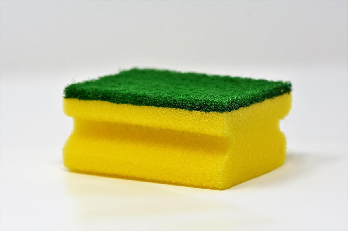 Éponge à récurer jaune avec une surface abrasive verte sur un fond blanc.