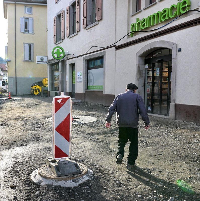 Rue du Rhône à Aigle avec des travaux de voirie en cours pour l’installation du chauffage à distance, bâtiments et pharmacie visibles.