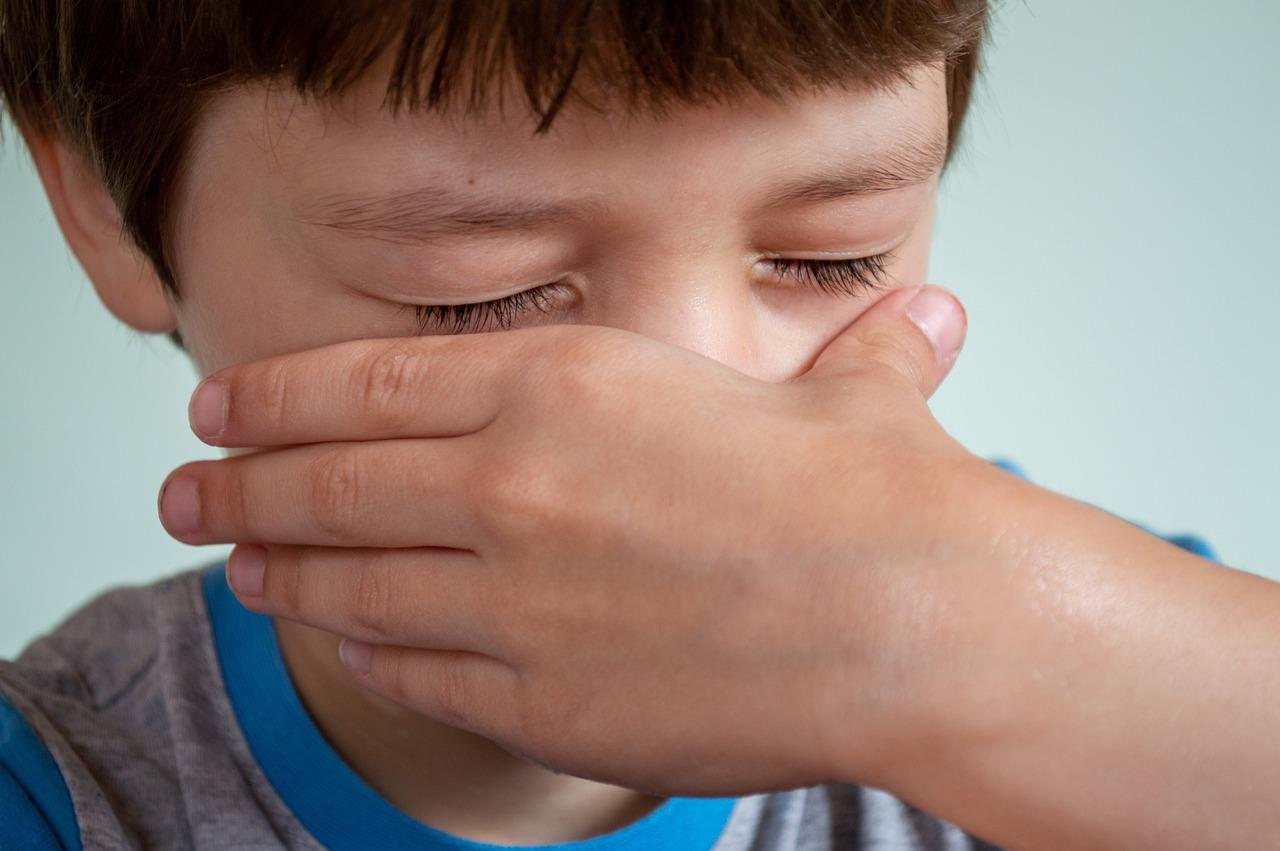 Enfant se couvrant le visage avec la main, yeux fermés.