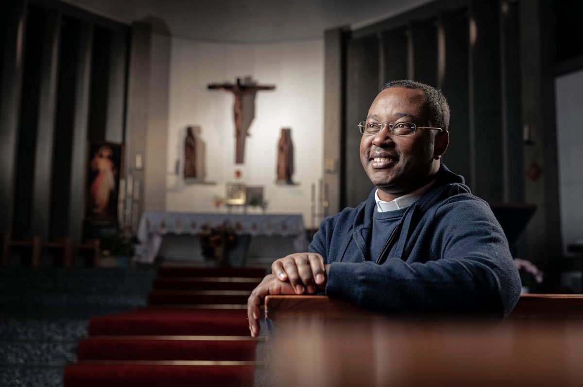 L’abbé Pontien Bushihi, souriant, pose dans l’église Saint Nicolas de Flüe, Chailly, devant l’autel et un grand crucifix.