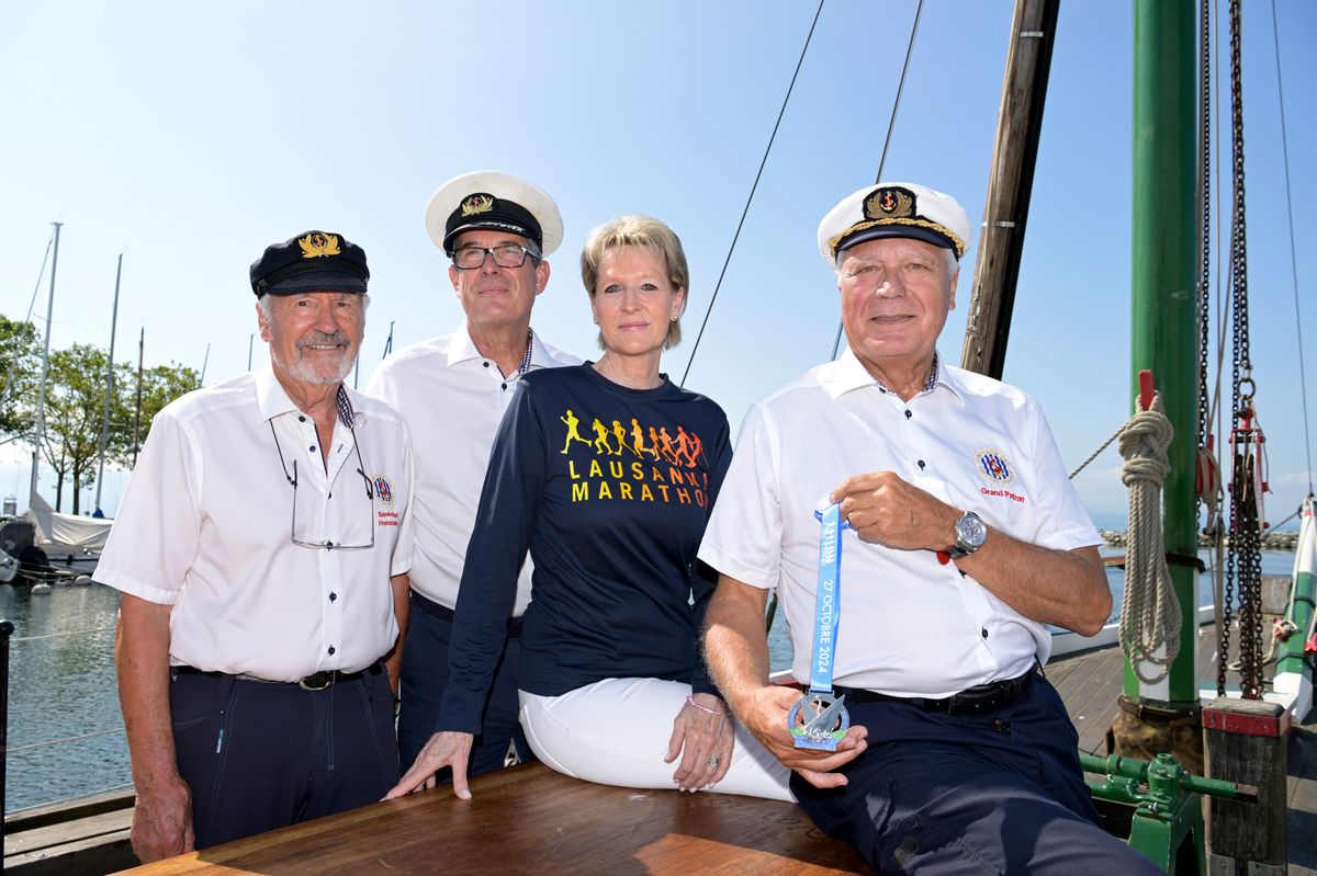Lausanne, le 20 août 2024. Quatre membres de la confrérie des Pirates, dont Josette Bruchez, posent avec la médaille de la Lausanne Marathon à l'effigie de la Vaudoise. Ils sont sur un bateau, avec des mâts et des voiles en arrière-plan. De g. à d. Roland Grunder, Andrea Christophe, Josette Bruchez et Gérard Hagemlocher.