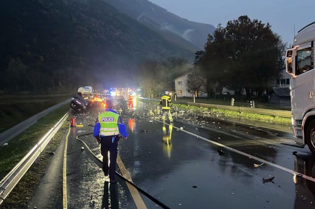 Accident à Loèche : site d’une collision entre une voiture et un camion avec des secours sur place, route mouillée et débris visibles.