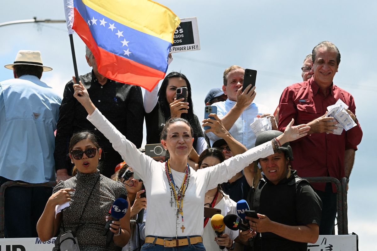 Venezuelan opposition leader Maria Corina Machado (C) holds a national flag atop a truck during a protest called by the opposition for election 'victory' to be recognised, in Caracas on August 17, 2024. Machado, who came out of hiding to attend the rally, vowed that anti-government protesters would remain out in force, as she addressed a protest in Caracas against Nicolas Maduro's disputed reelection victory claim. (Photo by Federico PARRA / AFP)