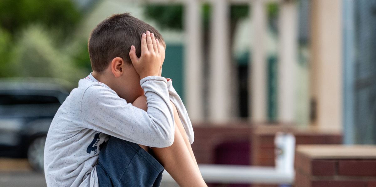 Enfant pleurant assis dans la cour d'école et se couvrant le visage.